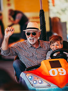 Grandfather and grandson having fun and spending good quality time together in amusement park. They enjoying and smiling while driving bumper car together.