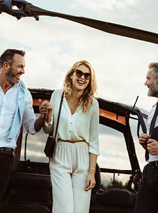 Beautiful woman escorted by her boyfriend out off a private helicopter with pilot standing by. Smiling couple traveling by their private helicopter.
